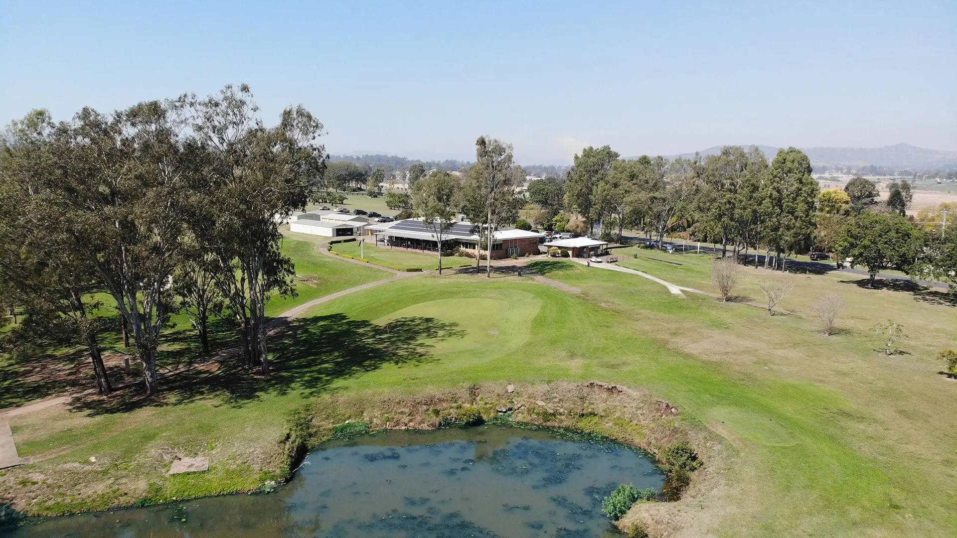 Aerial view of a green and pond with clubhouse behind