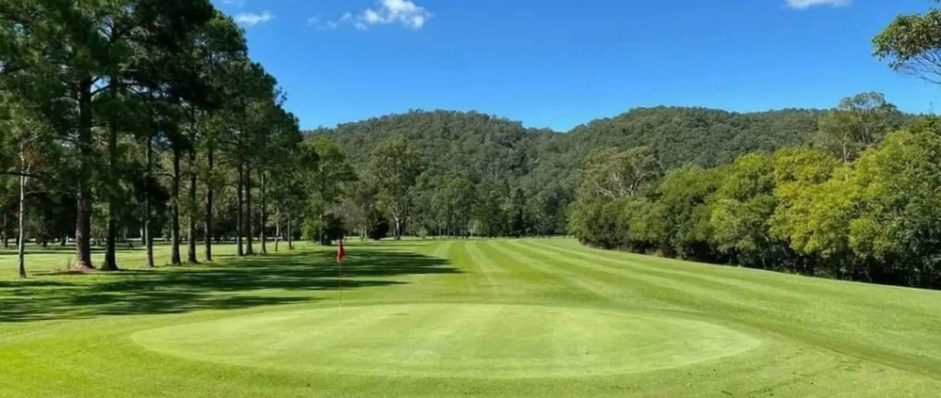 Green and fairway in front of forested hills