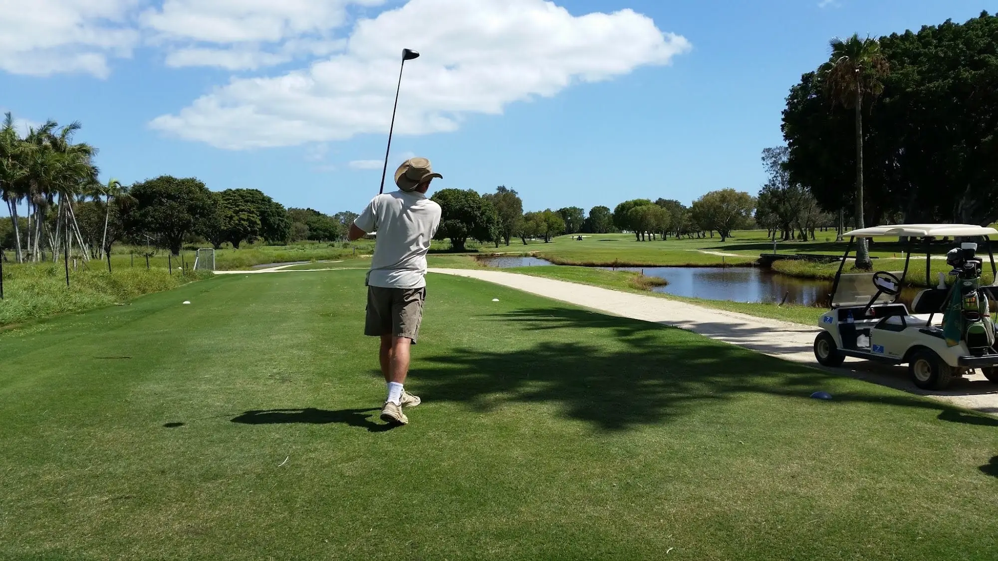 Golfer finishing a tee shot with a pond and fairway behind