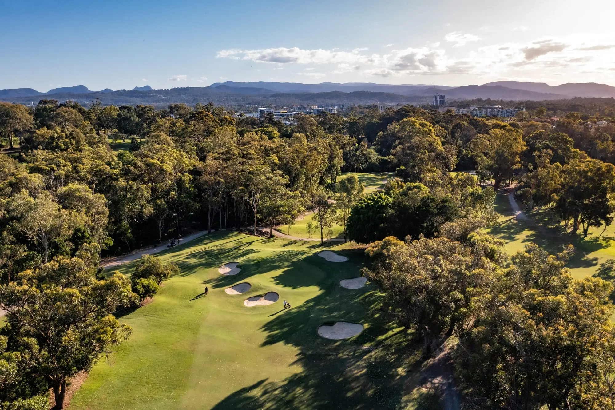 Aerial view of fairway and bunkers among trees with mountains beyond