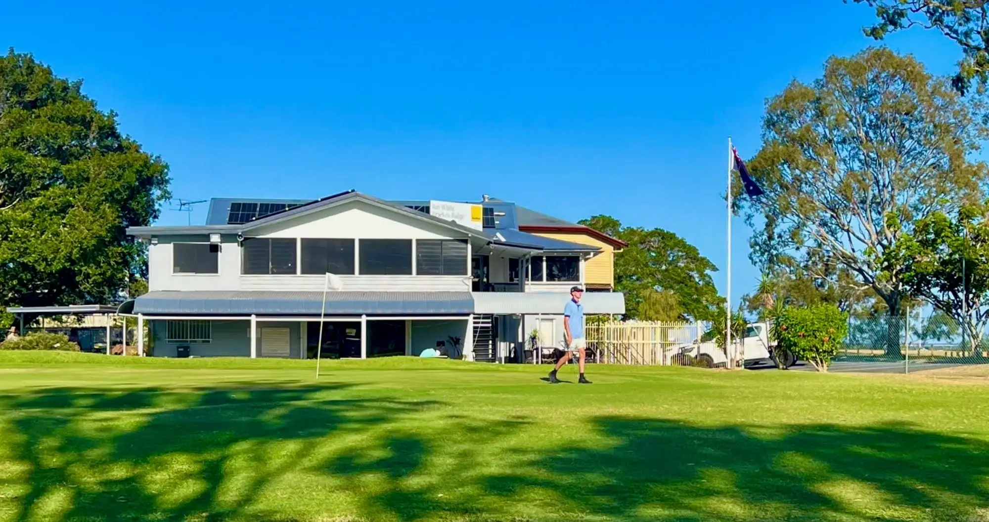 Clubhouse with flagpole behind a sunny green lawn