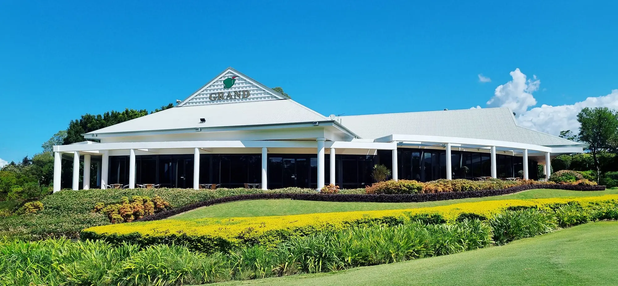 White clubhouse behind landscaped gardens and fairway