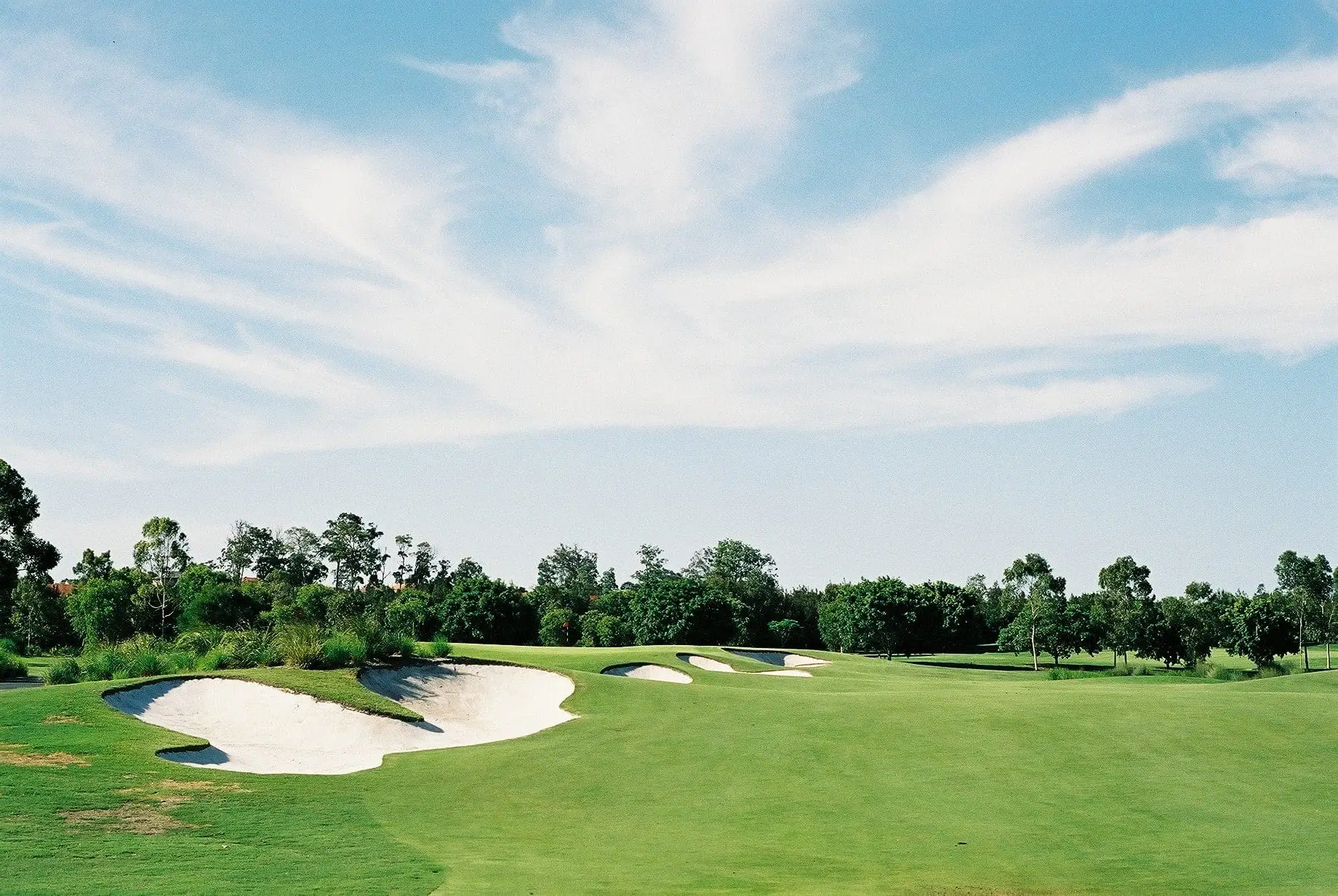 Wide fairway with large white bunker under streaked clouds