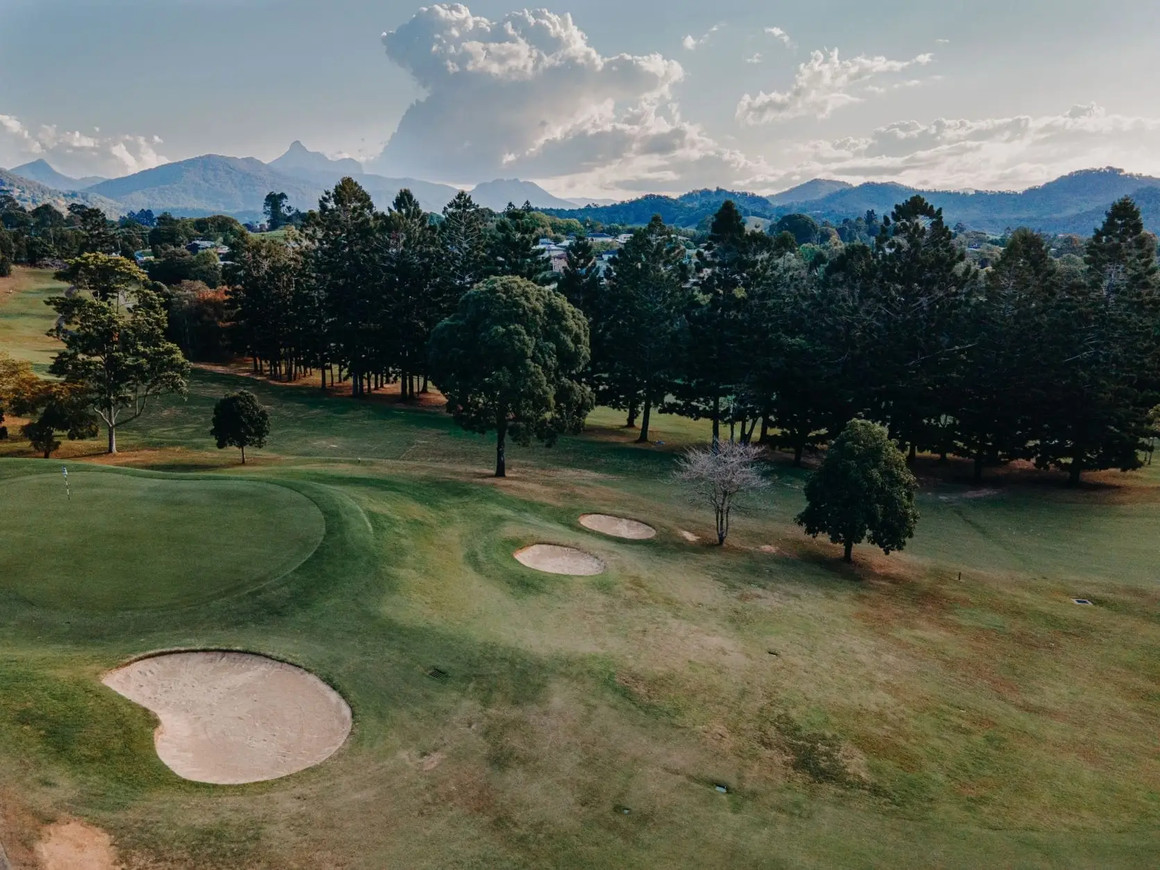 Green with bunkers and tall trees under mountain skyline
