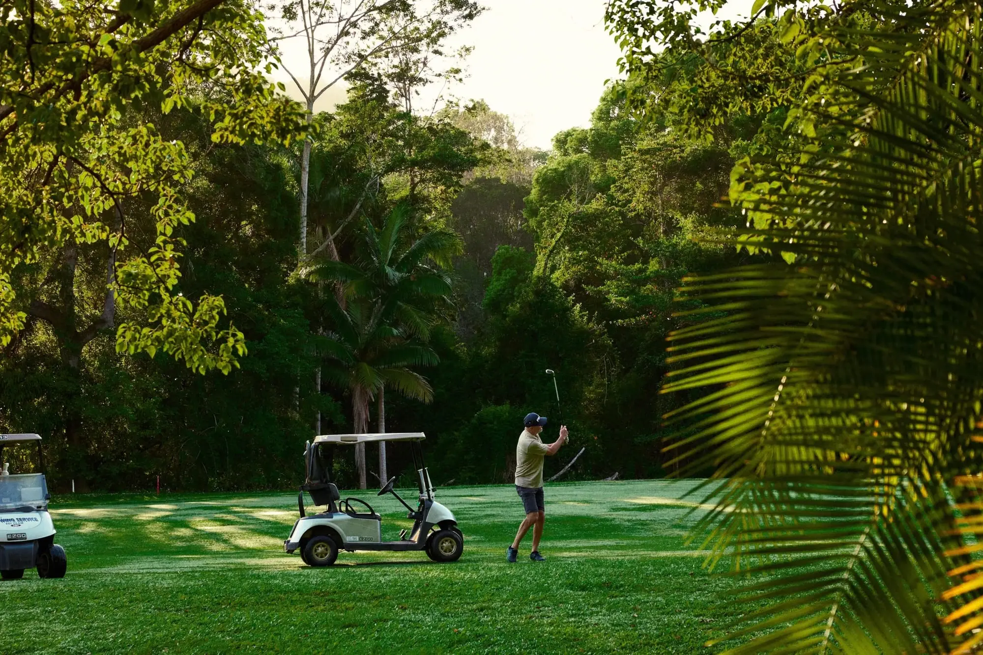 Golfer playing from a fairway surrounded by palms and lush foliage