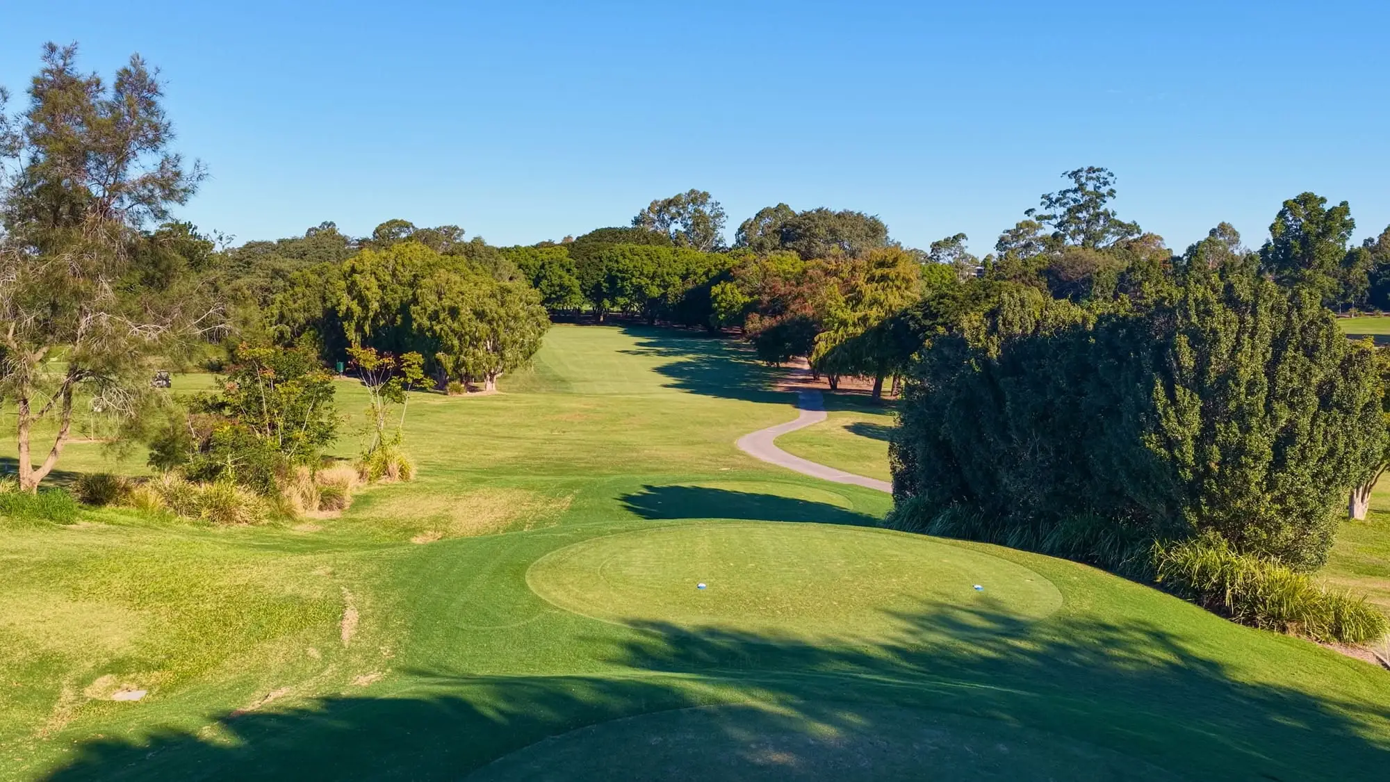Tree-lined fairway leading to a green under blue sky