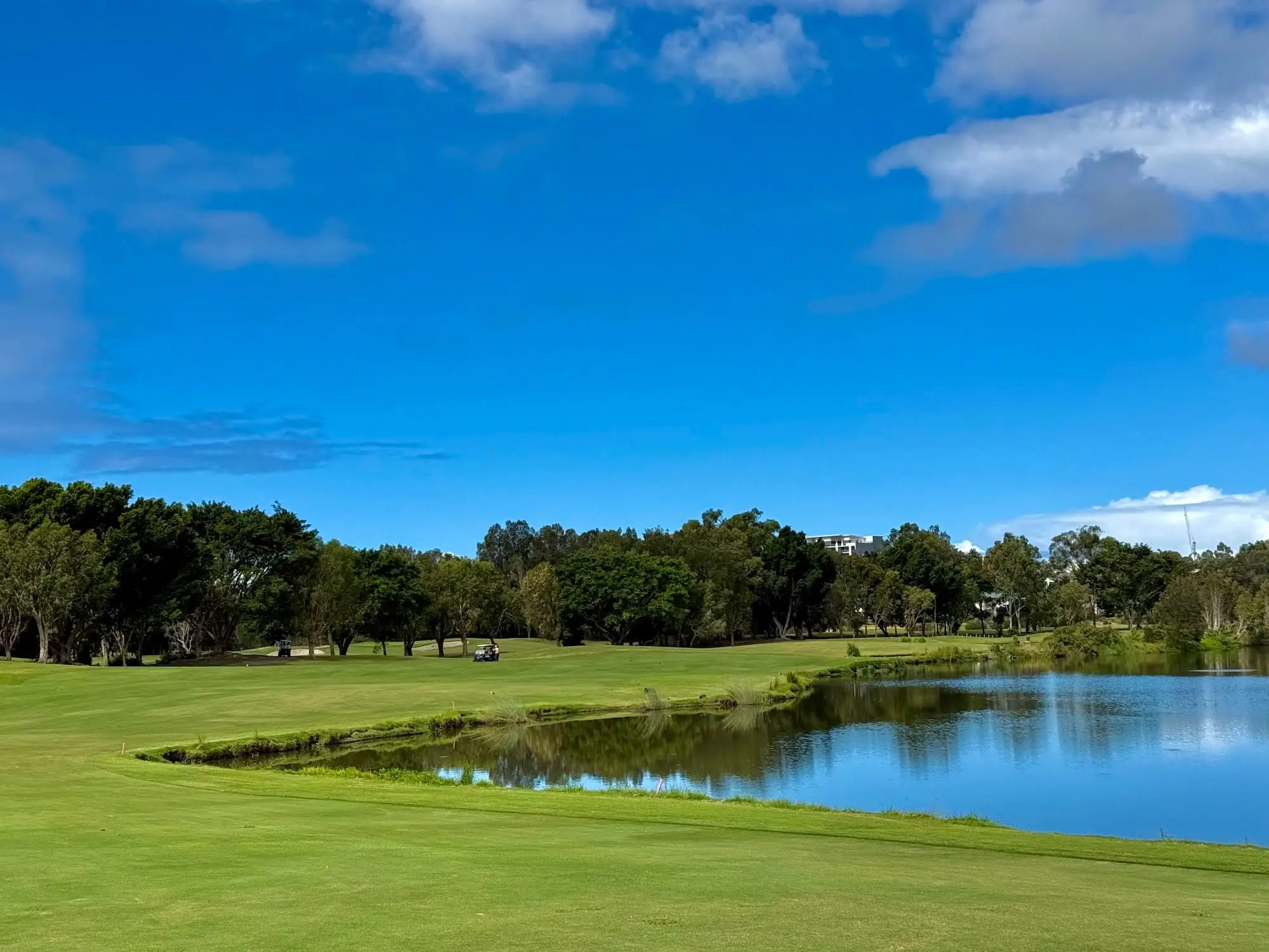 Lake beside a fairway with trees under a blue sky