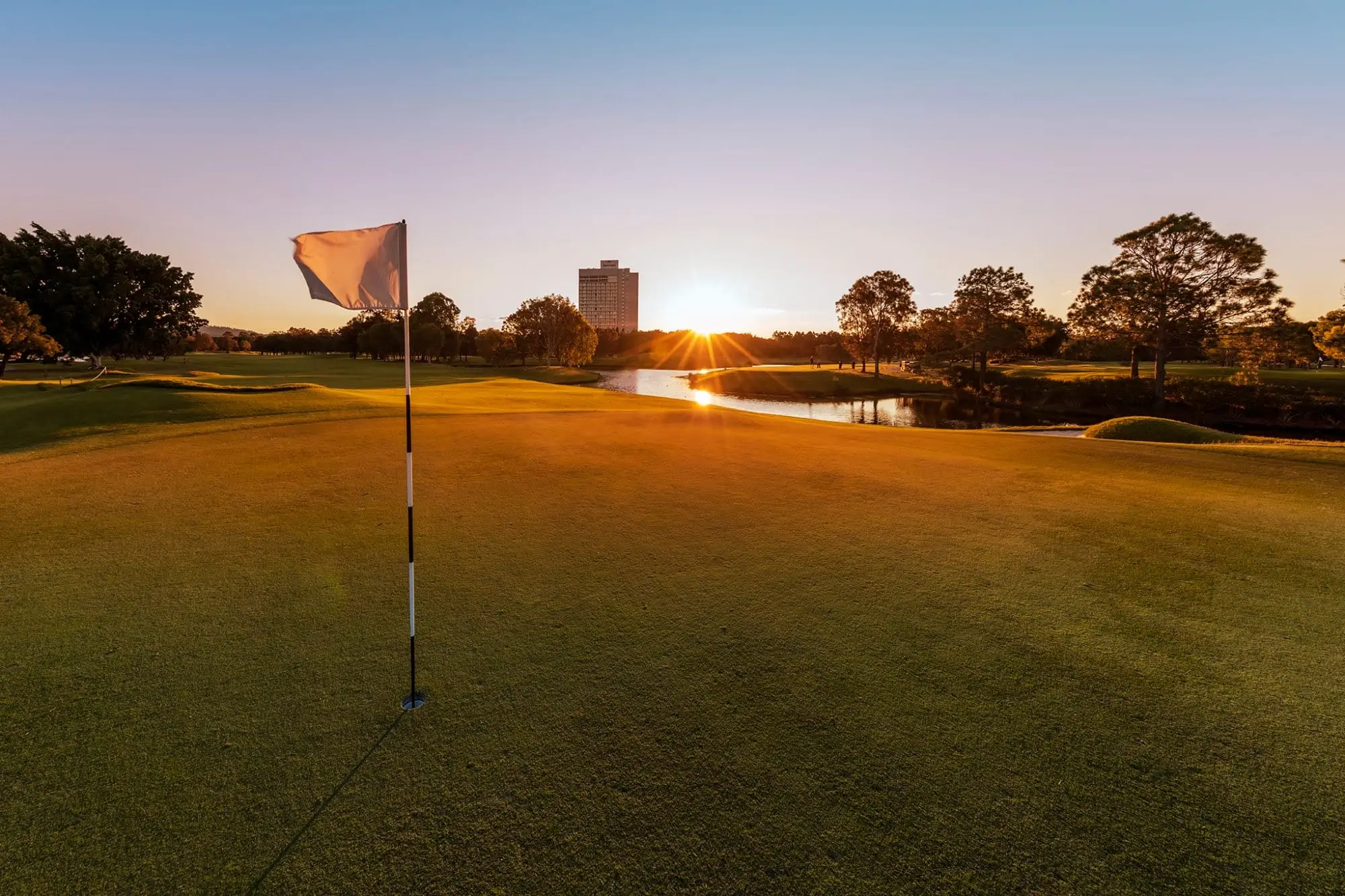 Flag on a green with sun setting over a lake