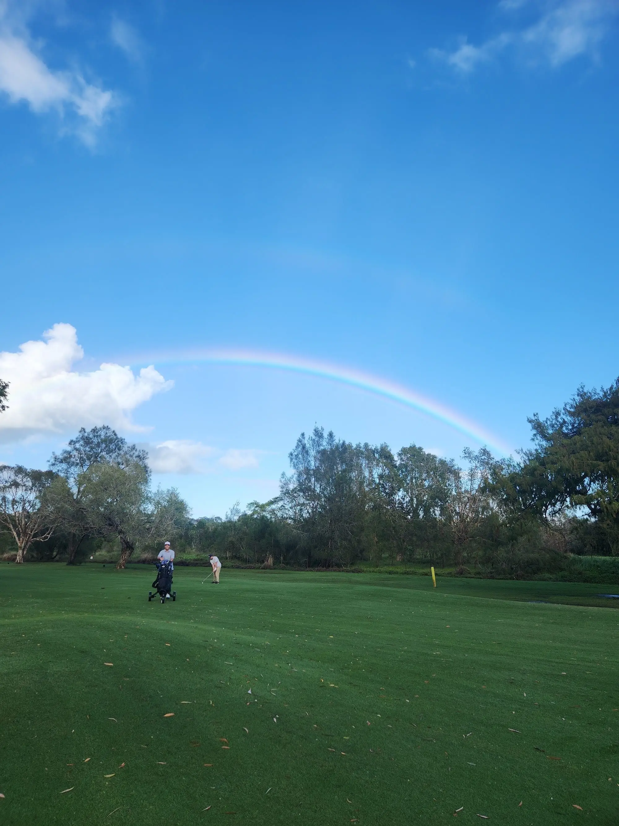 Rainbow over a fairway with trees and a golfer in the distance