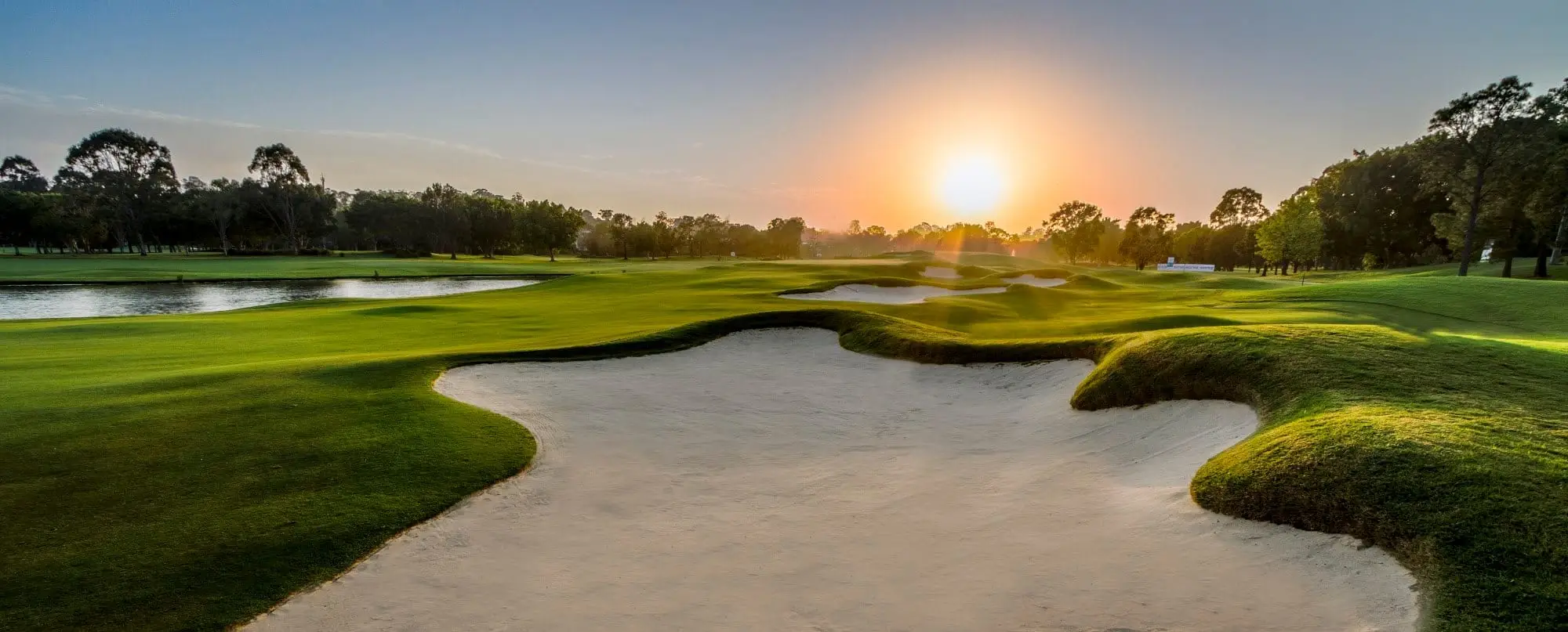 Sun setting behind a large sculpted bunker and fairway