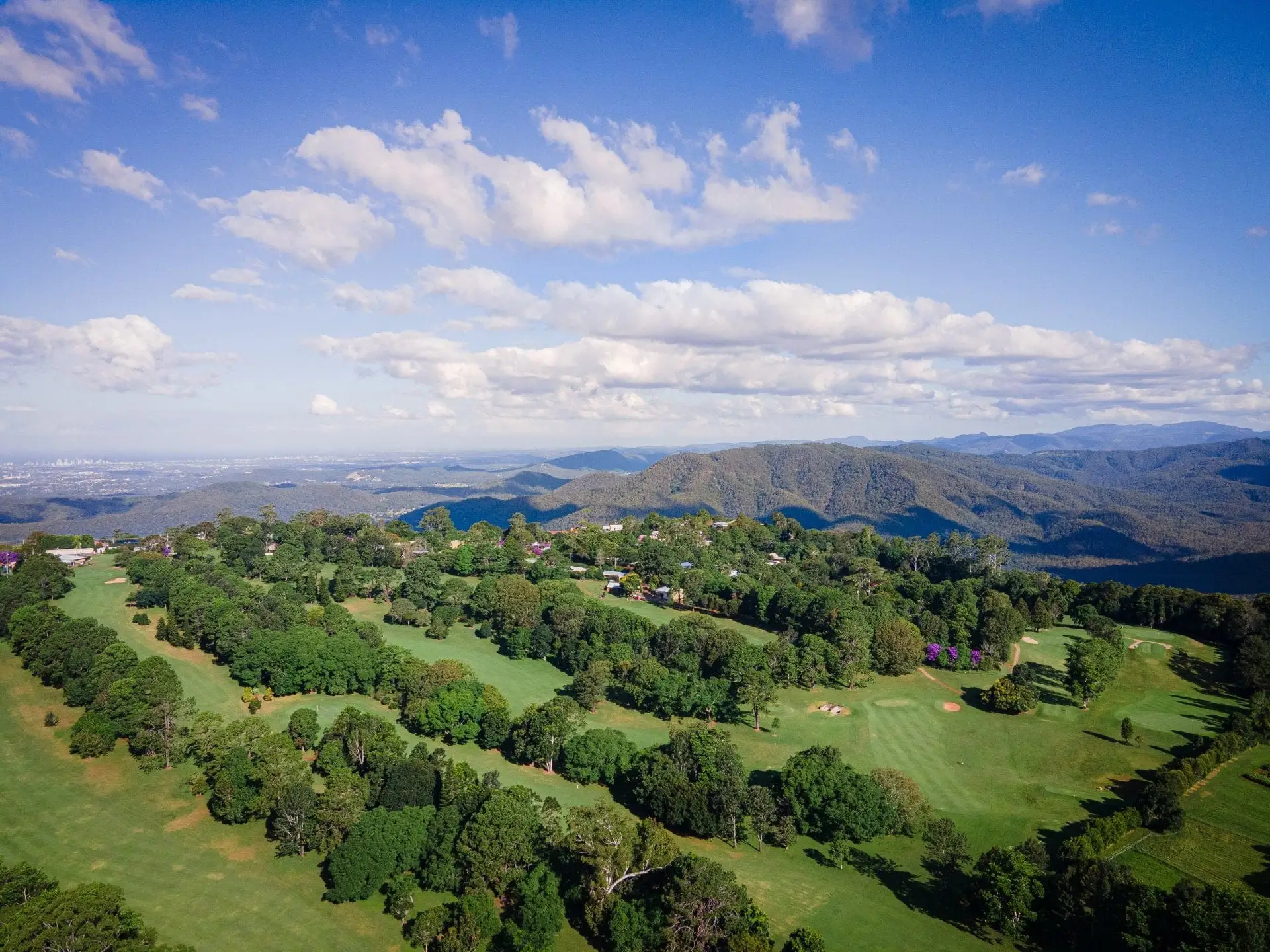 Aerial of course on forested mountain ridge with distant hills