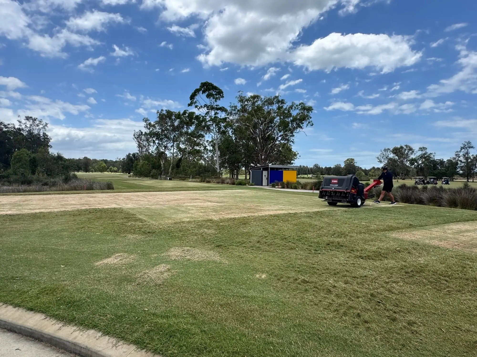 Fairway under blue sky with trees and a mower in distance