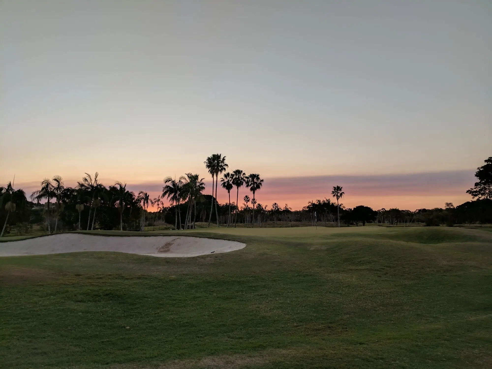 Bunker and fairway silhouetted by a pink sunset sky