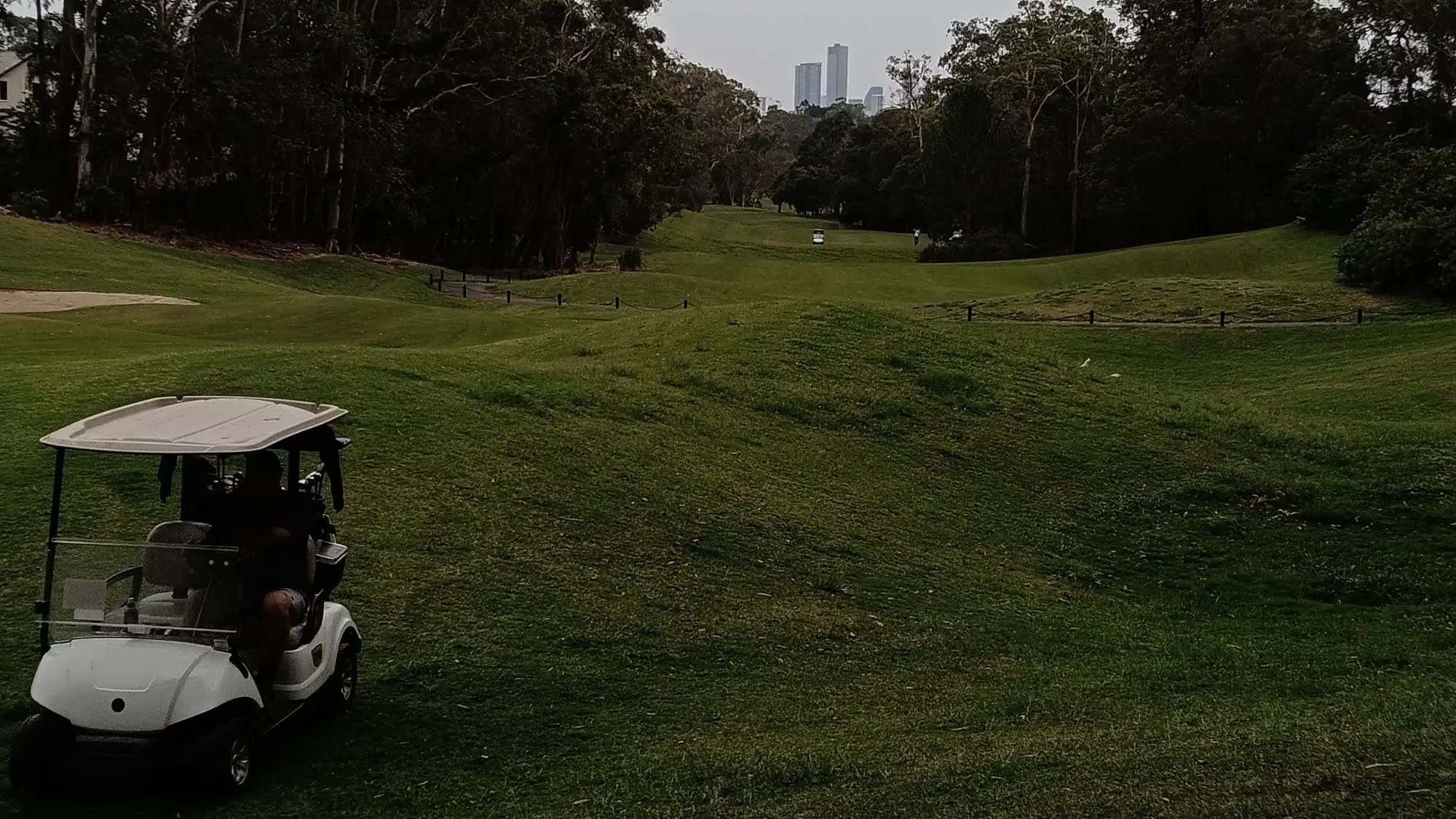 Fairway and bunker with distant city buildings through trees
