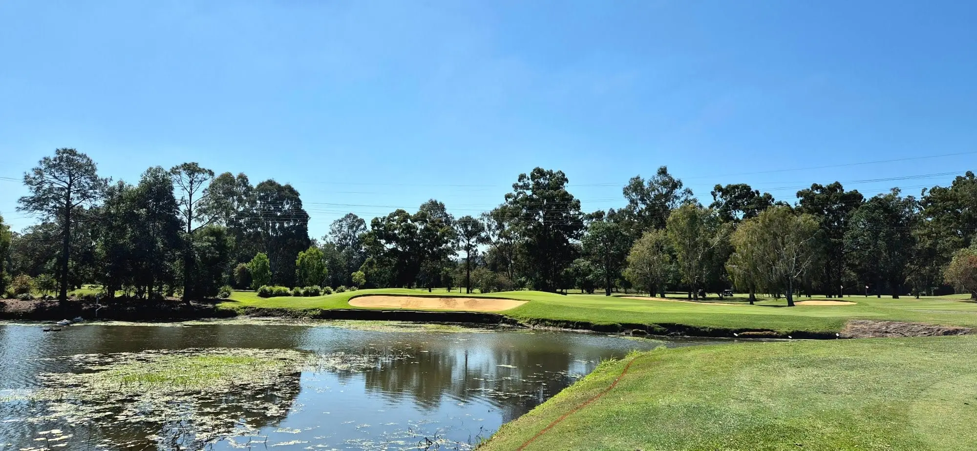 Pond with bunker and well-kept fairway under blue sky