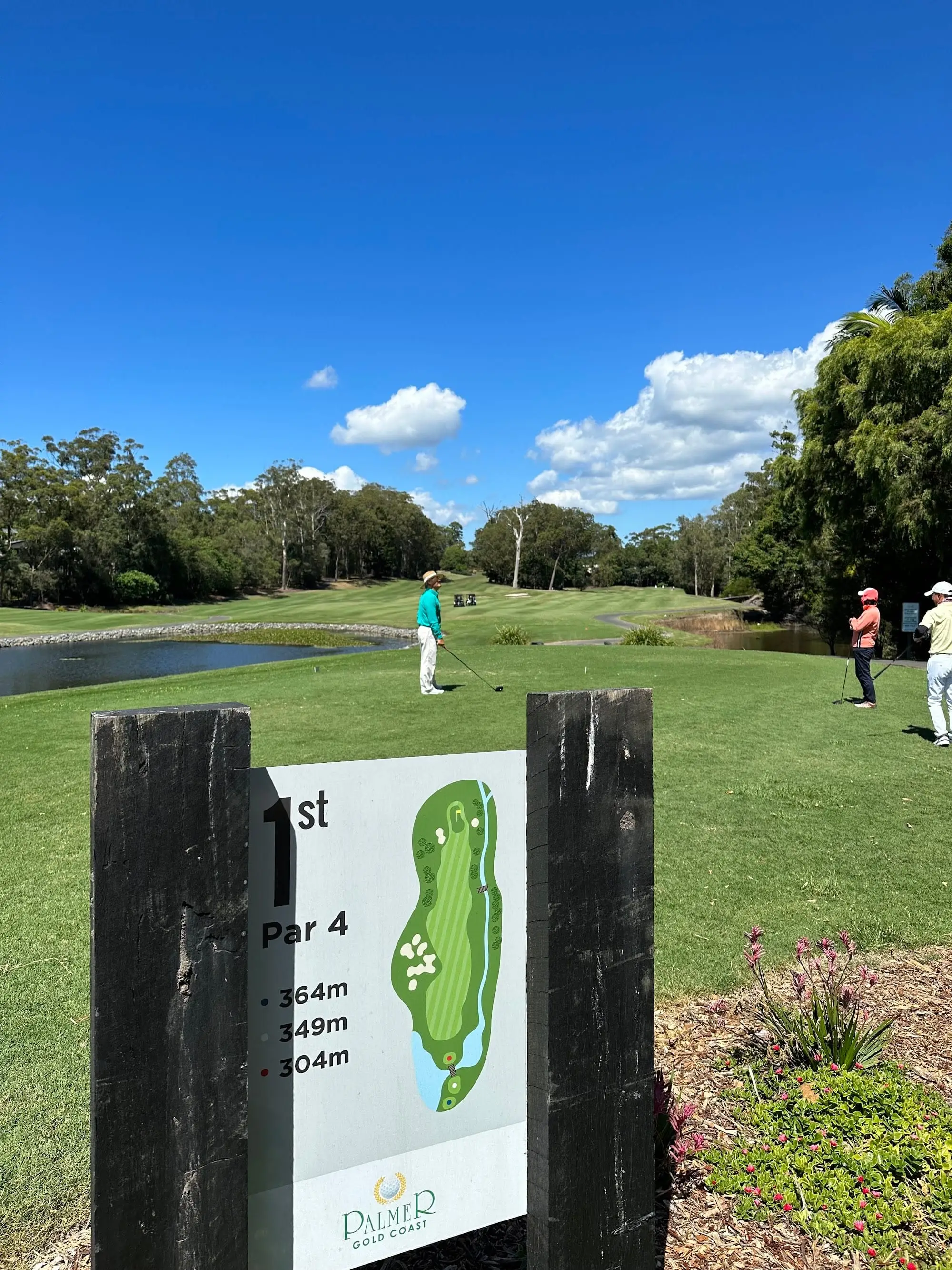 Golfers teeing off beside water at the first hole