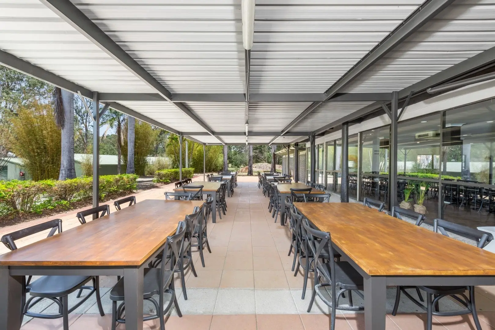 Covered outdoor dining terrace with long timber tables beside the course