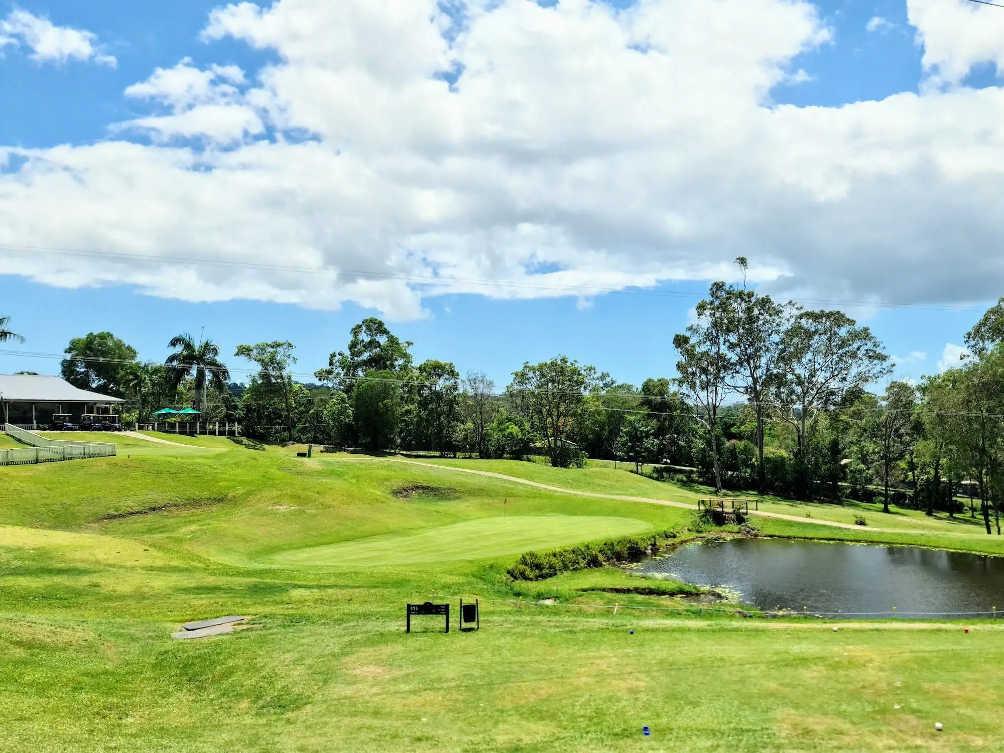Green beside a pond with trees and clubhouse in the distance