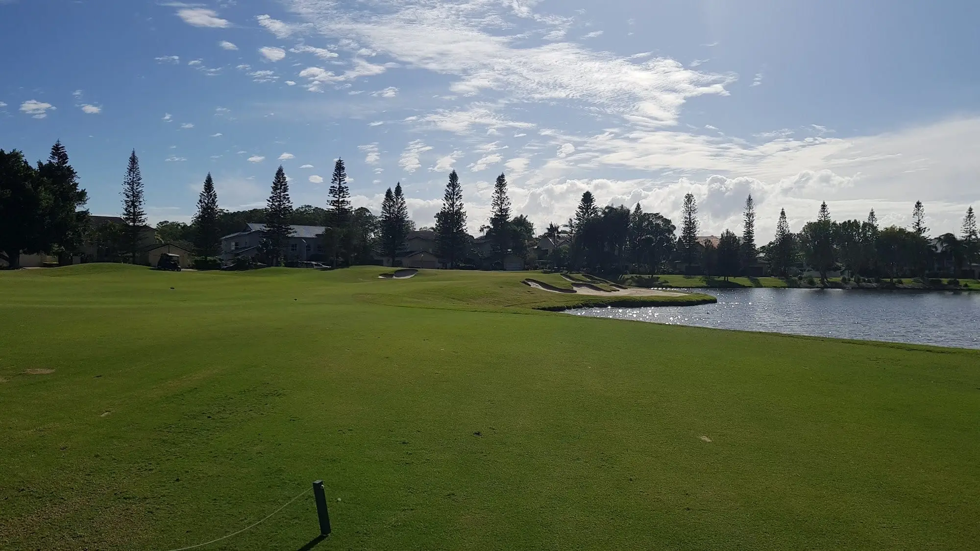 Fairway running beside a lake with pines and blue sky