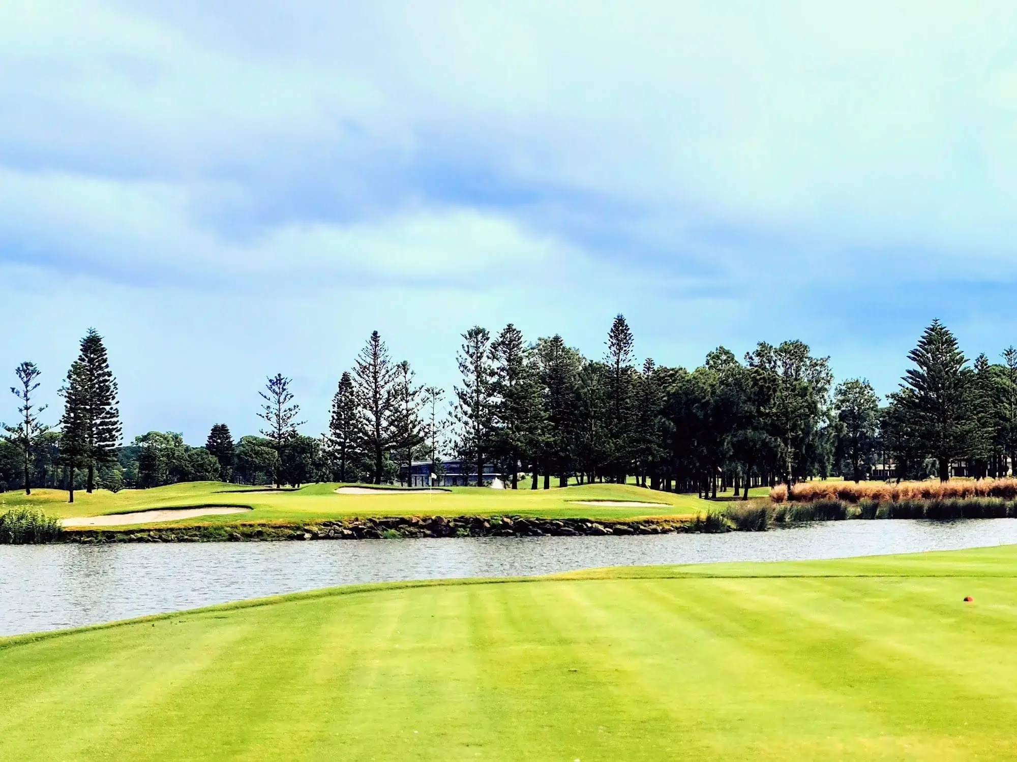 Fairway and bunker across a lake lined with pines
