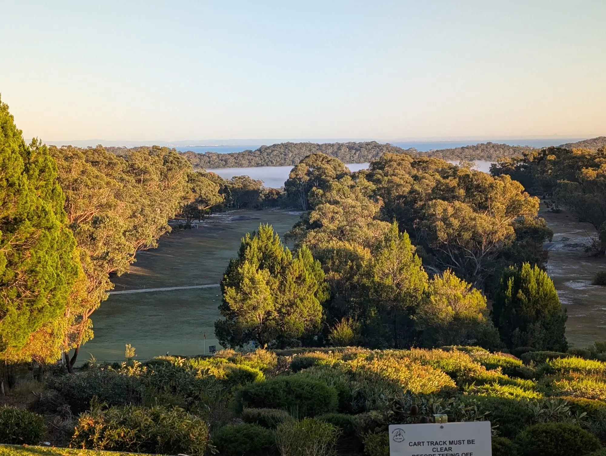 Fairway and bush with water in the distance at sunset