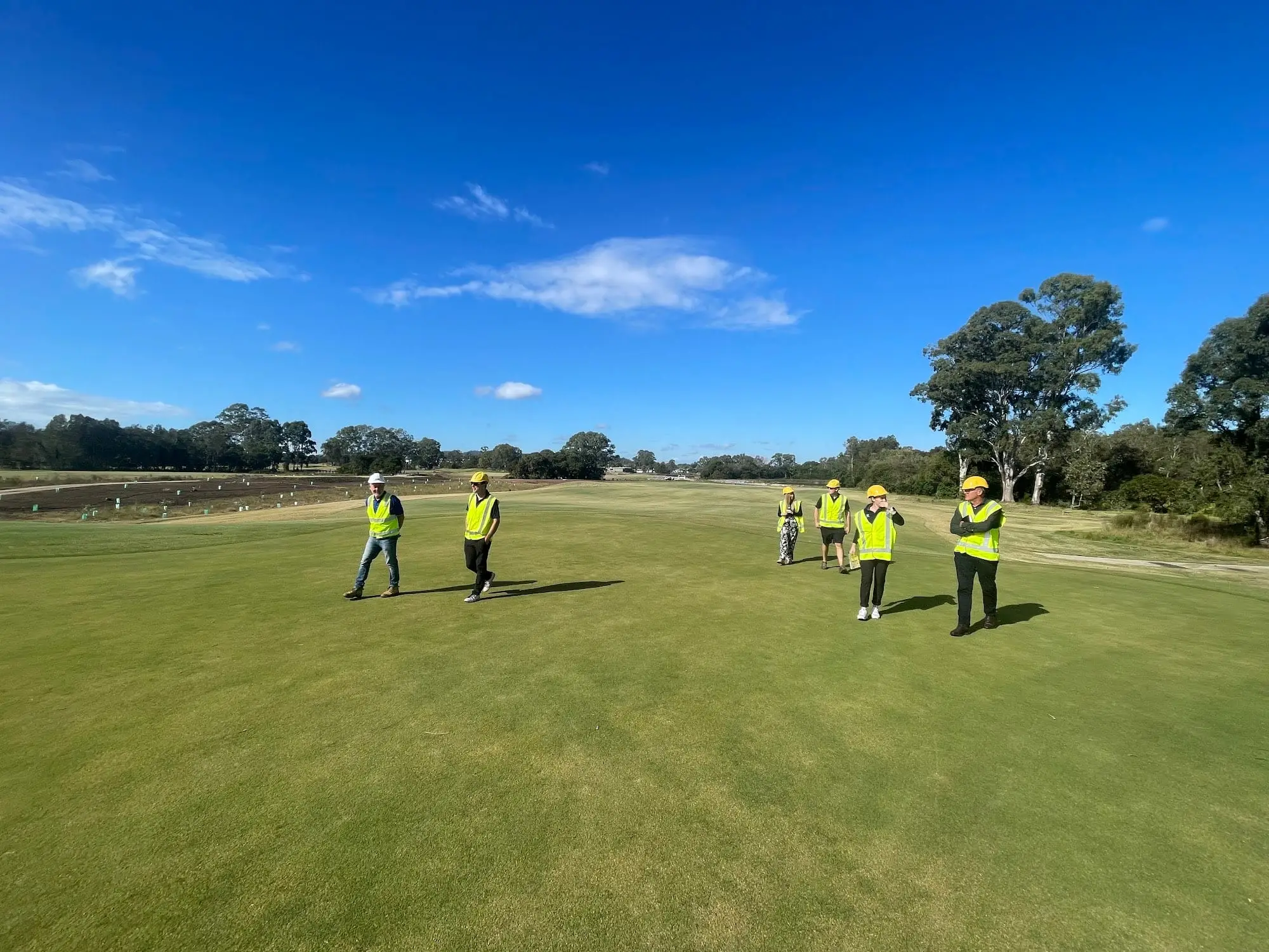 Open fairway under blue sky with greenkeepers in the distance