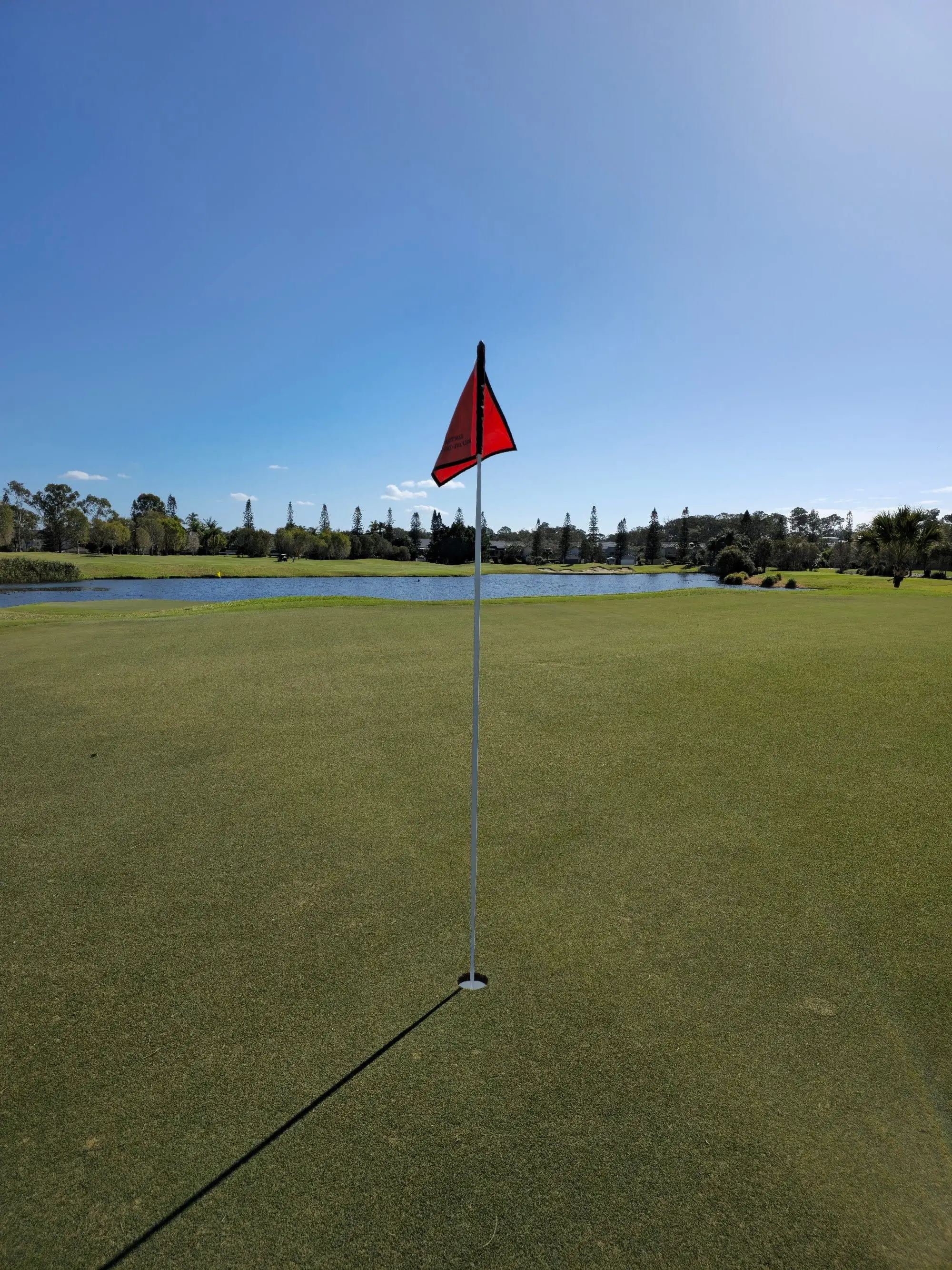 Red flag on a green beside a lake under blue sky