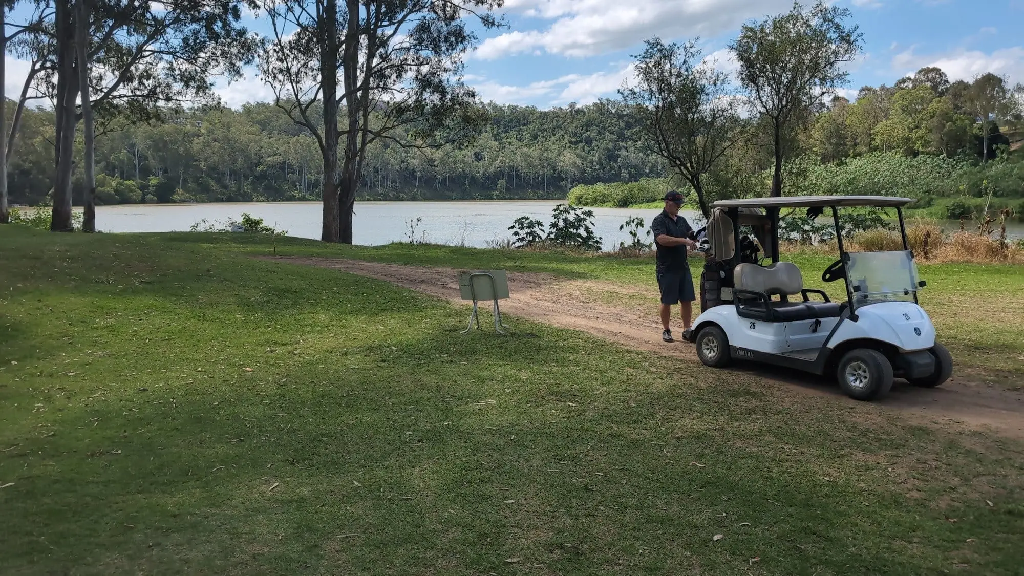 Golf buggy beside a tee overlooking a lake and bushland