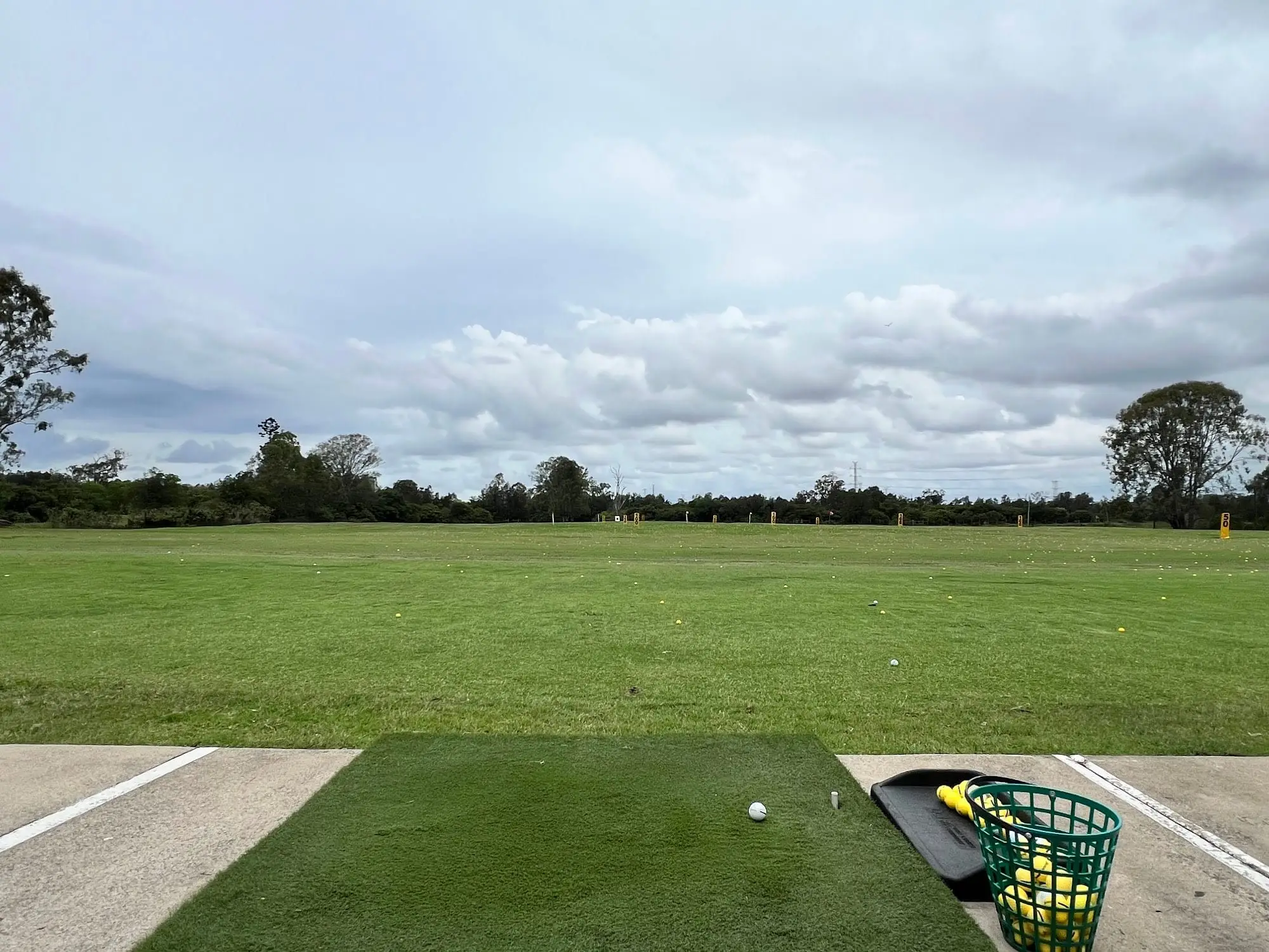 Driving range turf and hitting mat under a cloudy sky