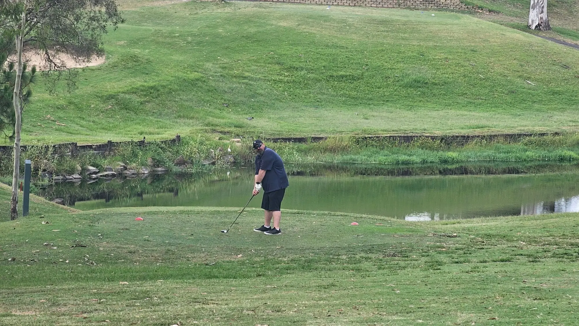 Golfer on a tee beside a pond with grassy bank