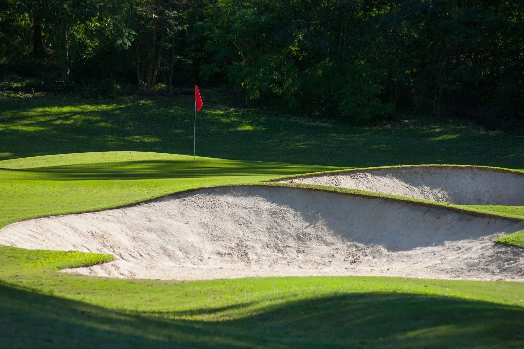 Large white bunker below a green with red flag