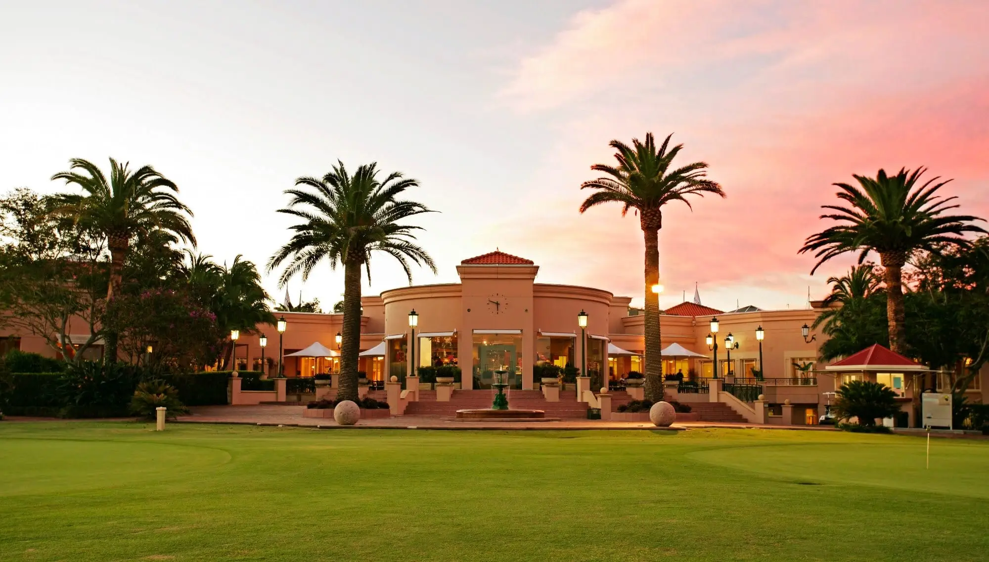 Mediterranean-style clubhouse with palms at sunset behind the fairway