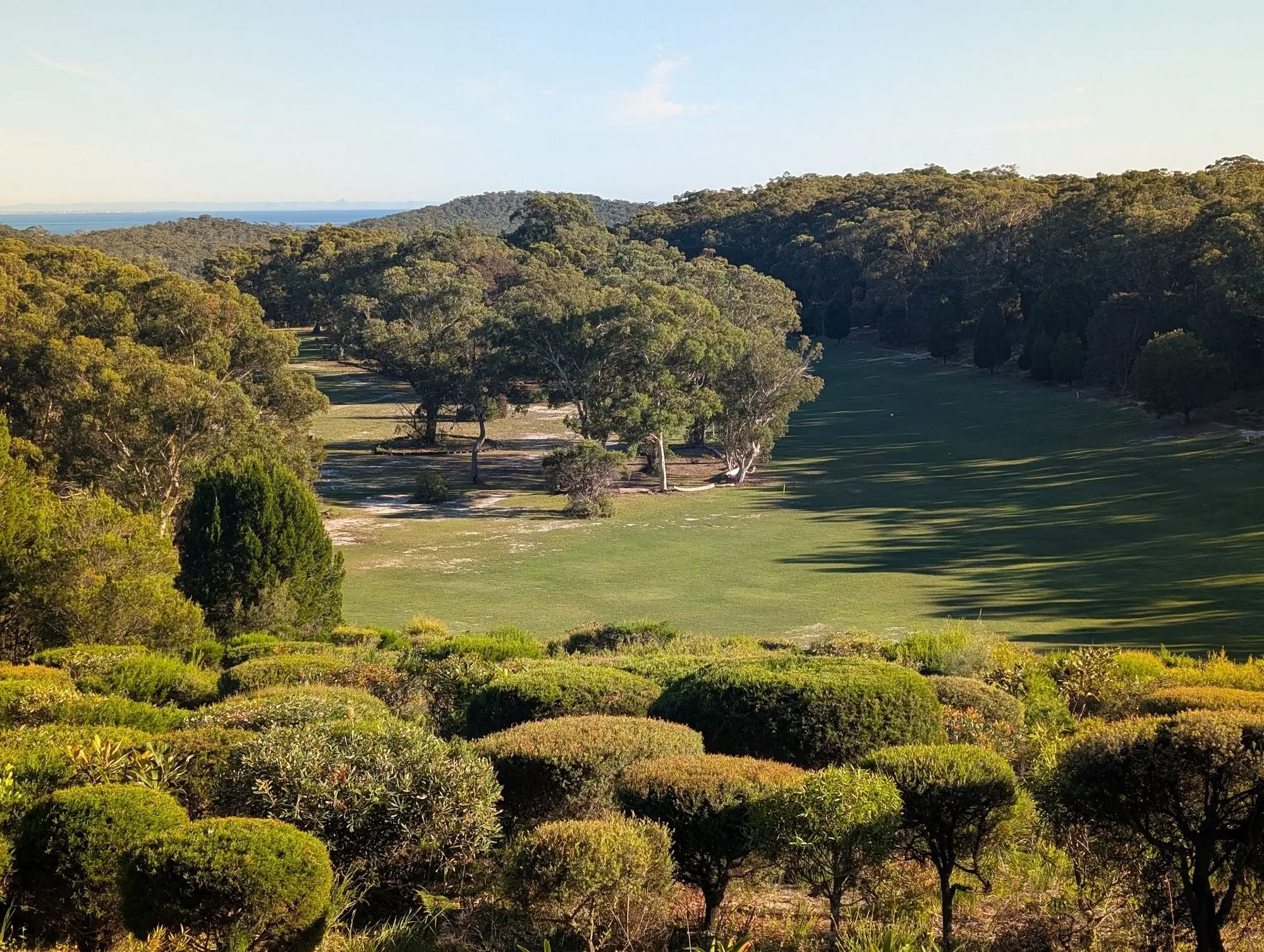 Valley fairway seen from above with bushland and water beyond