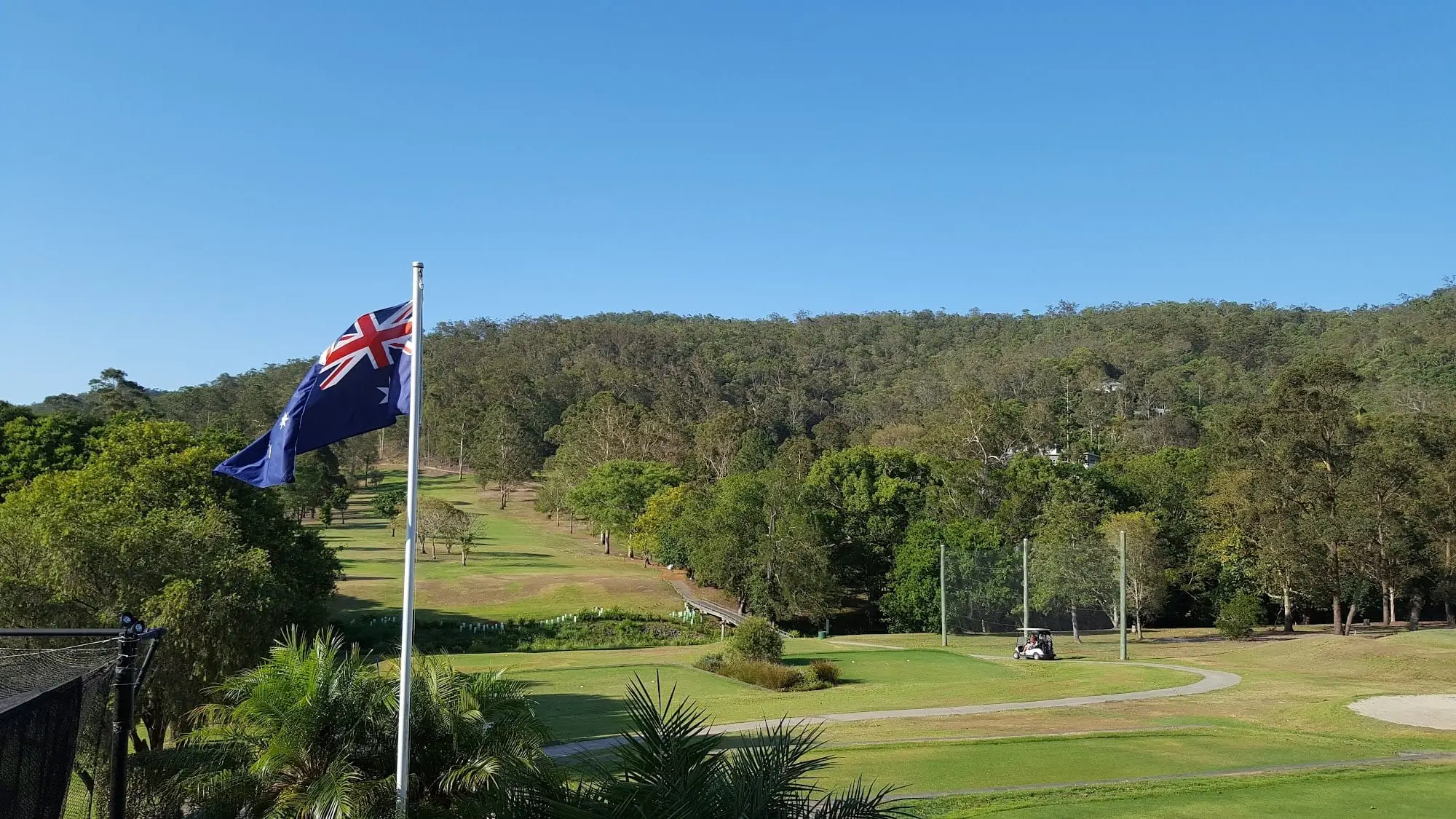 Flag flying above fairway and driving range with forested hills beyond