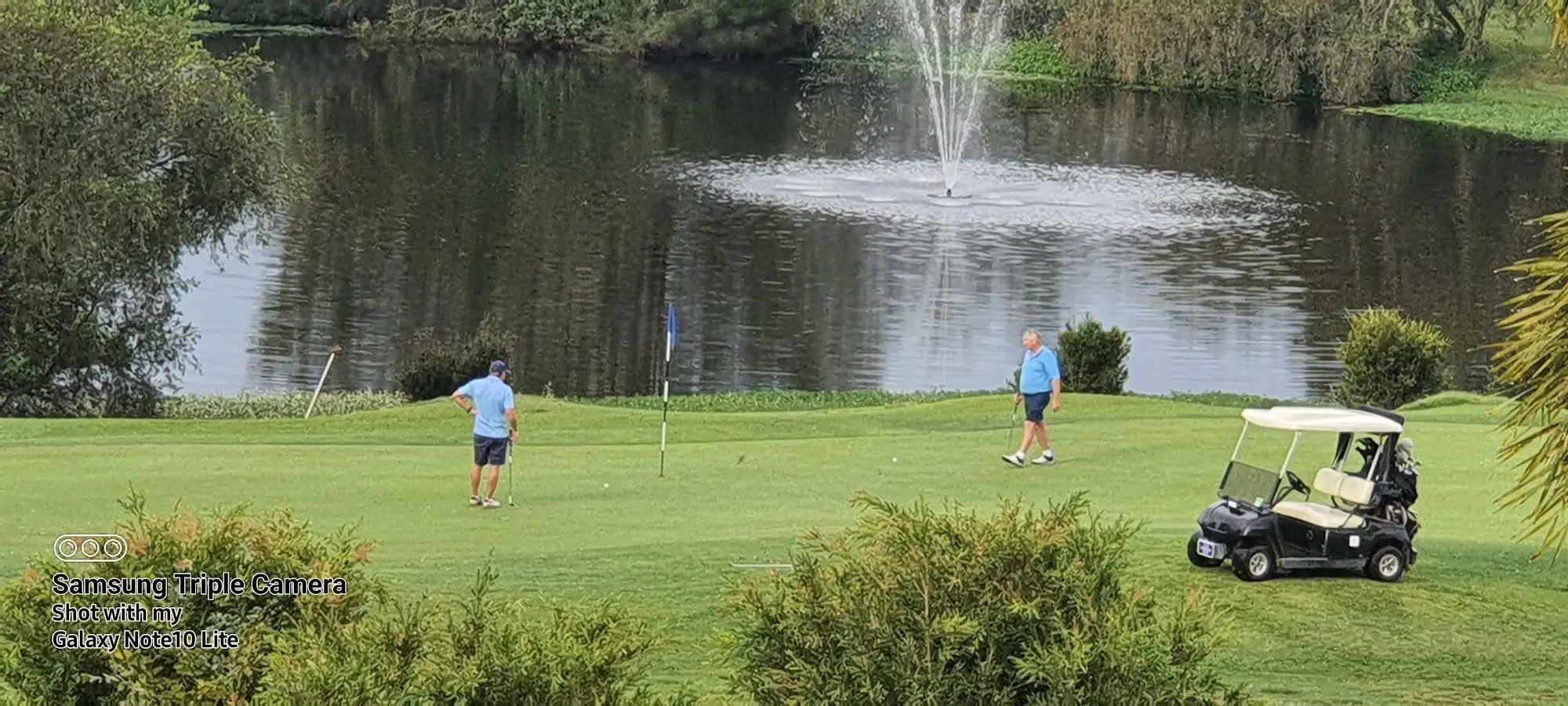 Fountain in a lake behind a green with golfers
