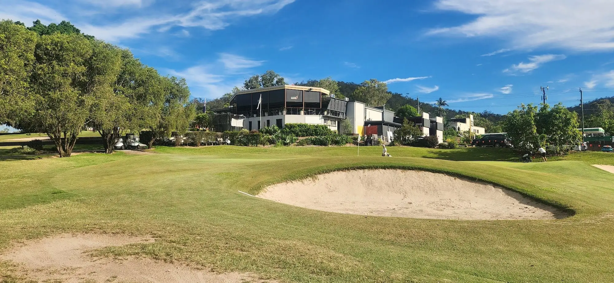 Bunker beside a fairway with clubhouse buildings in the distance