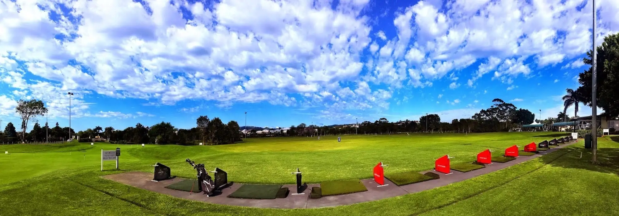 Driving range with tee mats under a bright cloudy sky