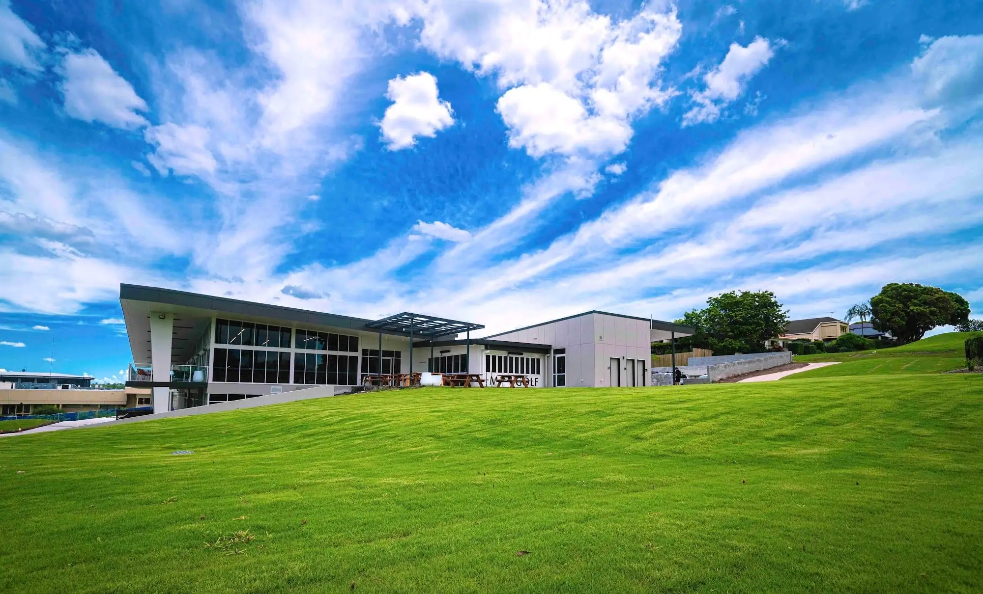 Modern clubhouse behind a green lawn under dramatic sky