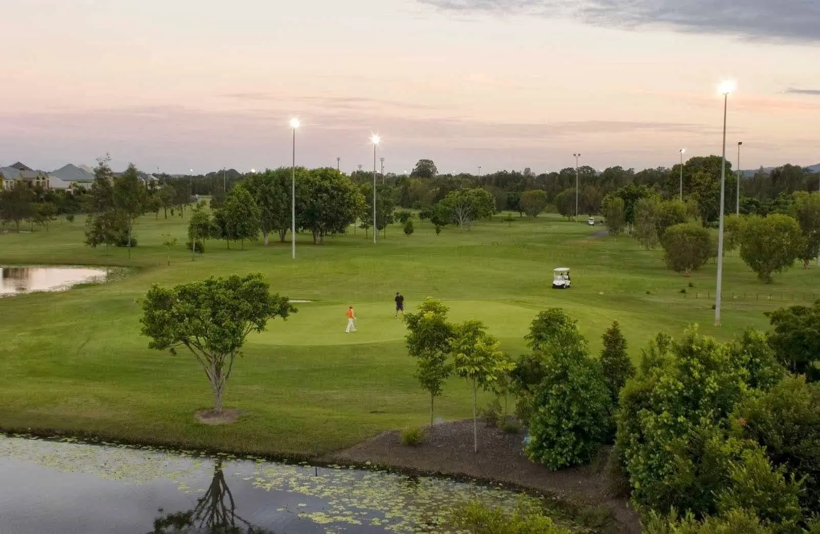 Fairway with ponds and floodlights at dusk, trees around