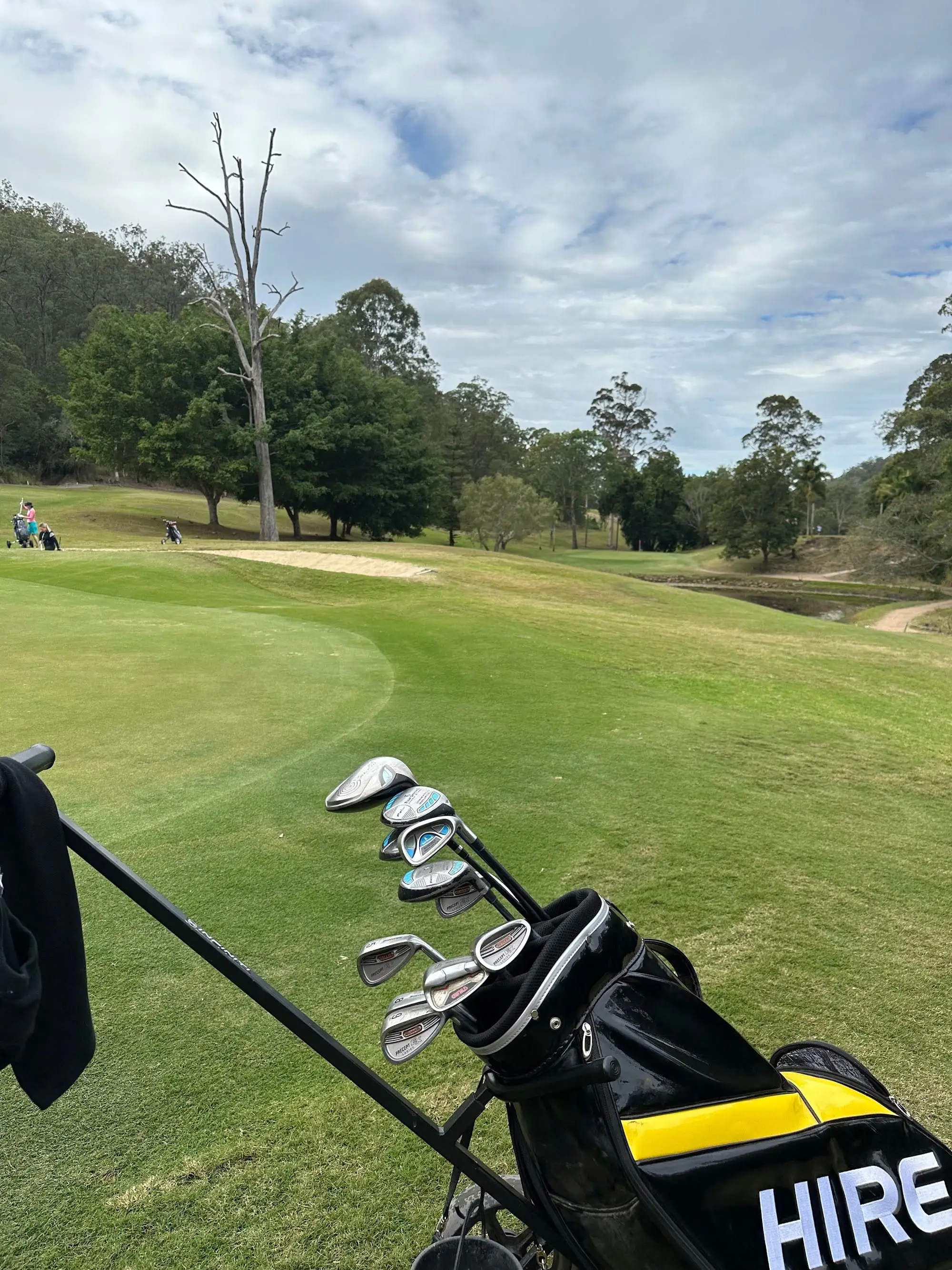Fairway curving past a bunker and pond under tree-lined hills