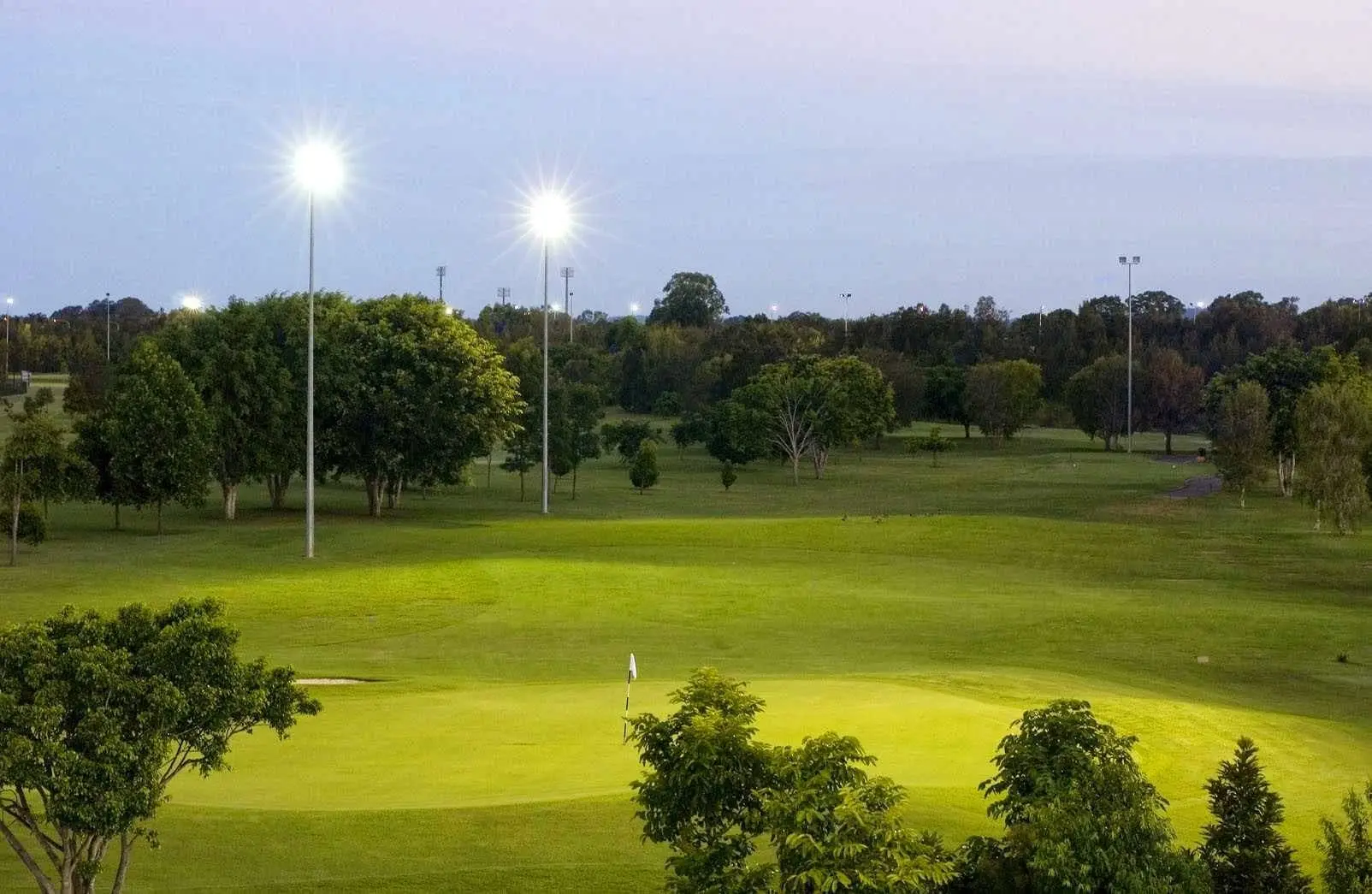 Floodlit green and fairway at twilight surrounded by trees