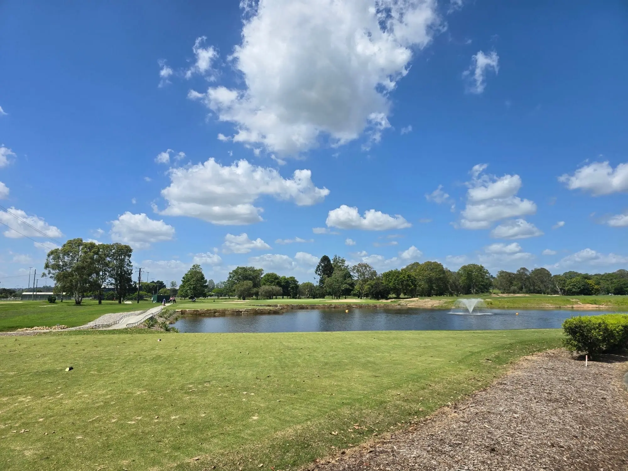 Lake with fountain across a fairway under puffy clouds