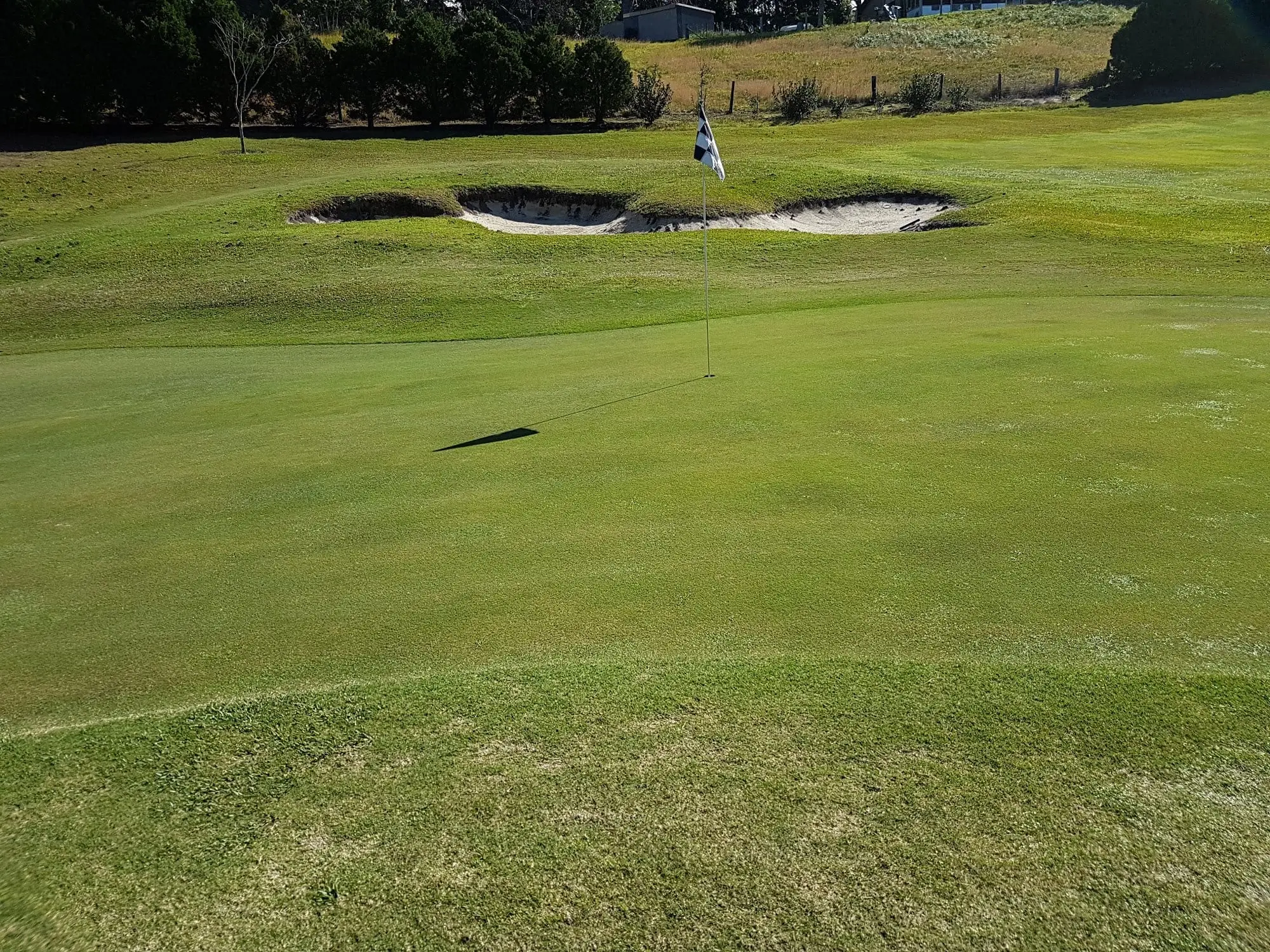 Green with two bunkers on a sloping fairway