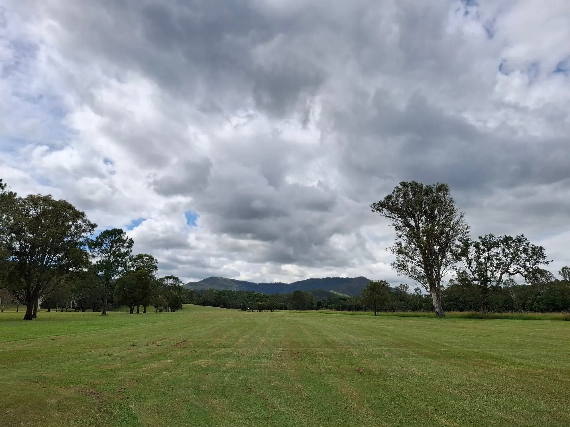 Wide mown fairway under cloudy sky with mountain backdrop
