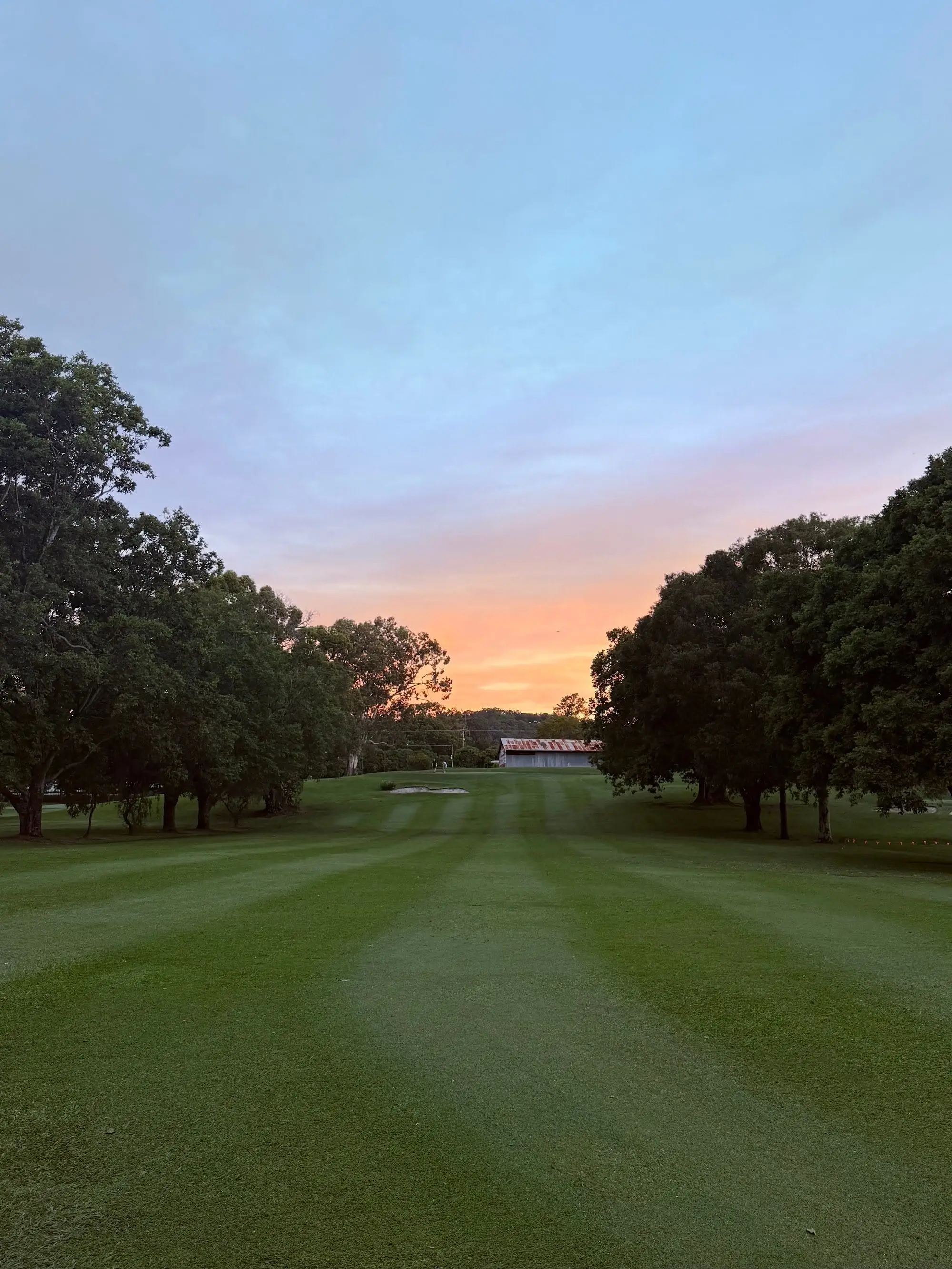 Mown fairway at dusk with orange sky and clubhouse ahead